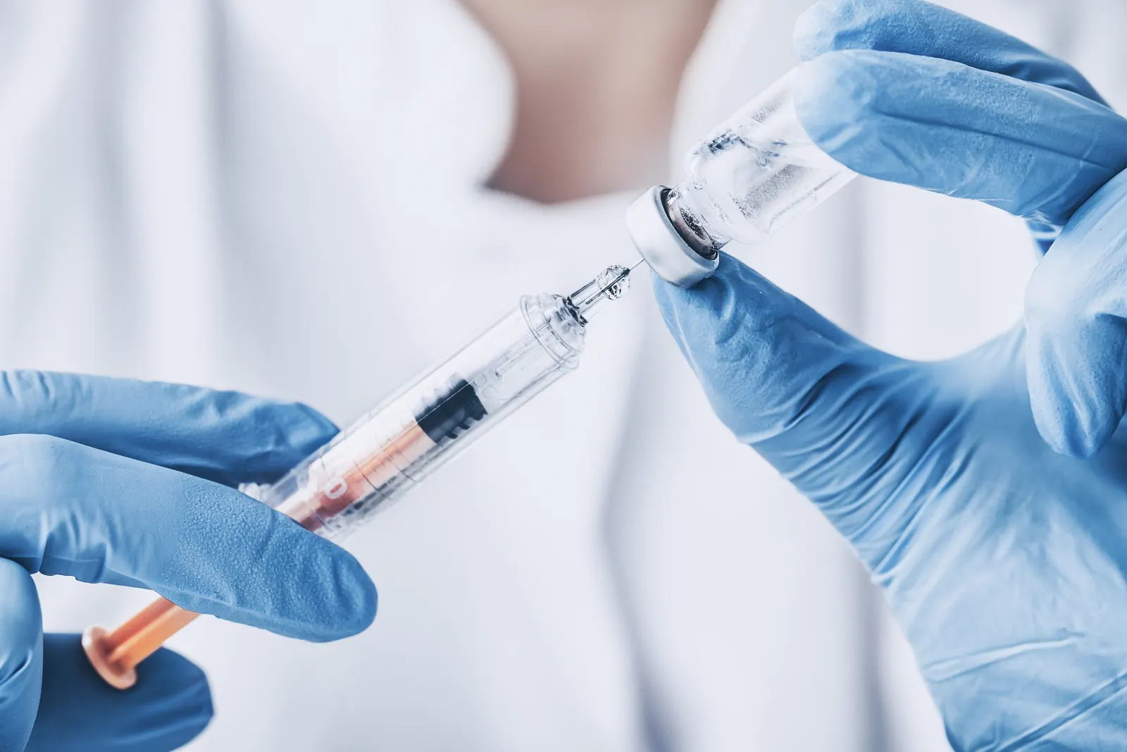 Gloved hands filling a syringe from a vial