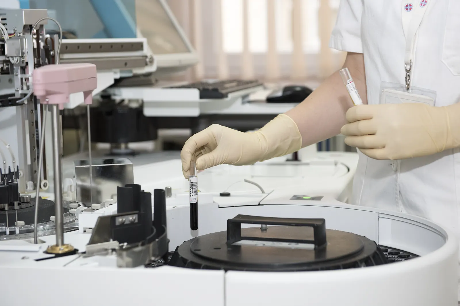Laboratory technician placing a blood sample tube into an analyser
